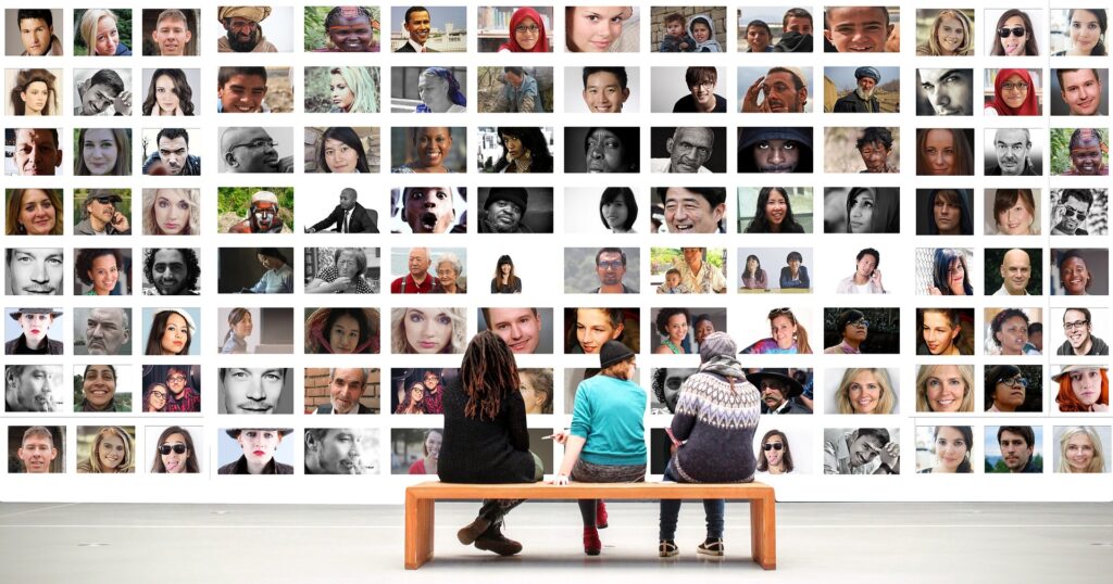 three people sitting in a museum looking at a wall of people's faces